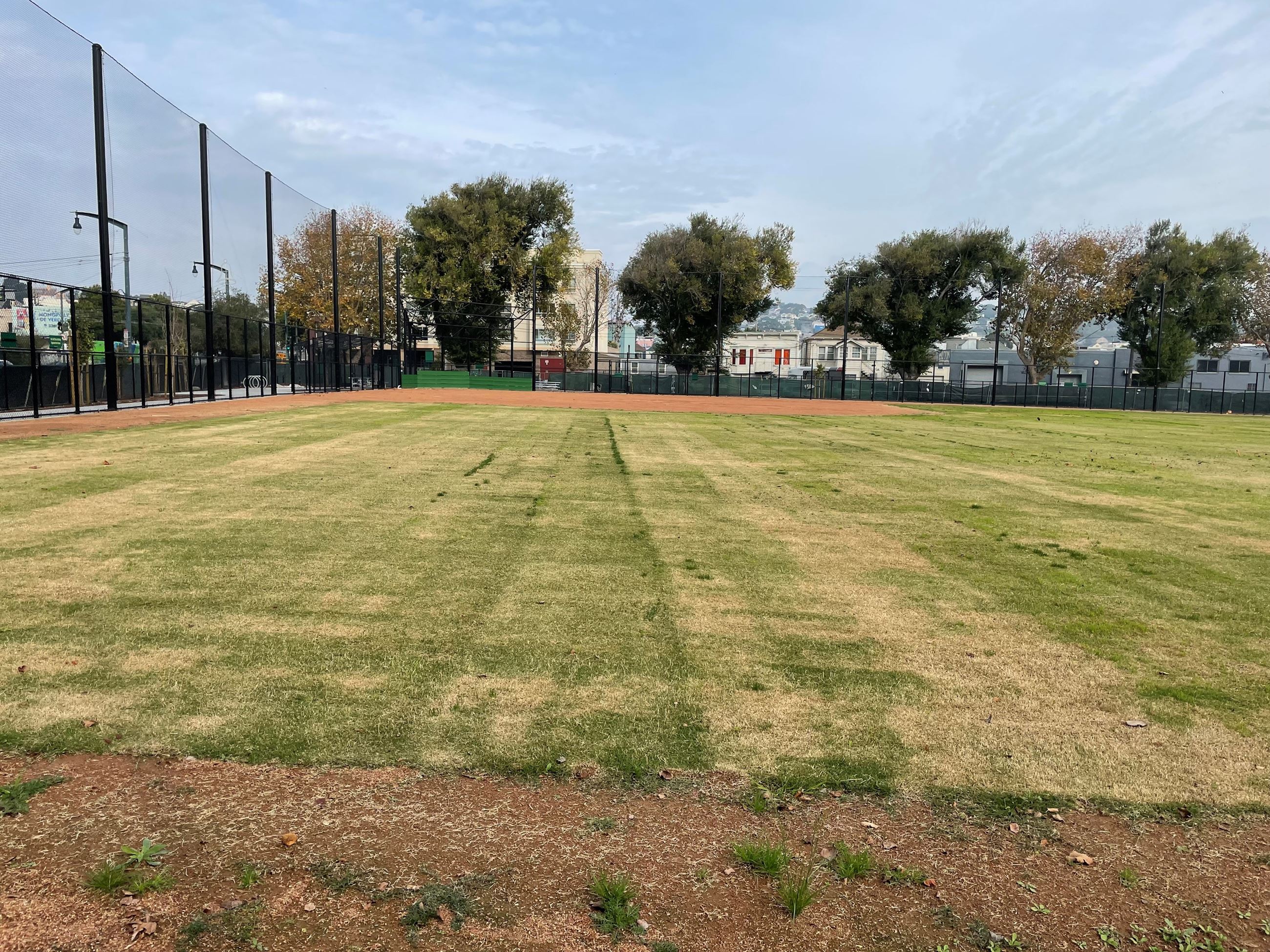 View from outfield of new ballfield toward home plate. Tall black fencing on the left of the field.