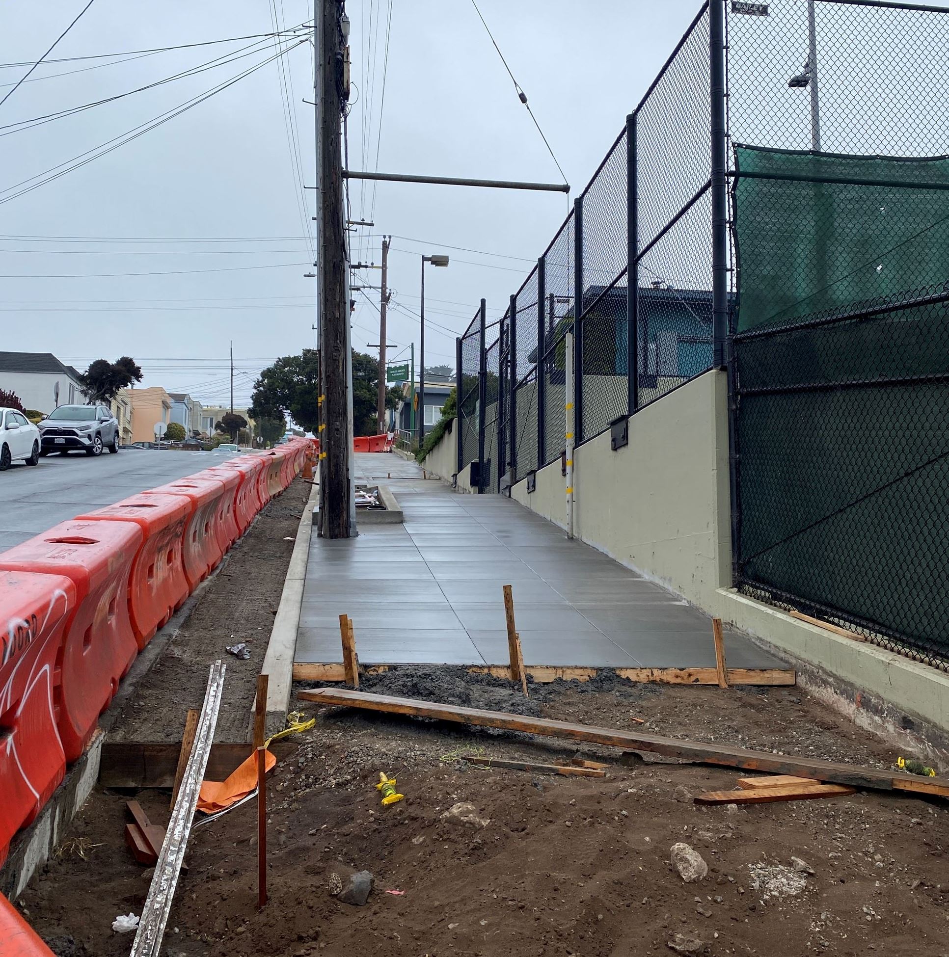 Large orange barricades to the left blocking the freshly poured concrete and open soil