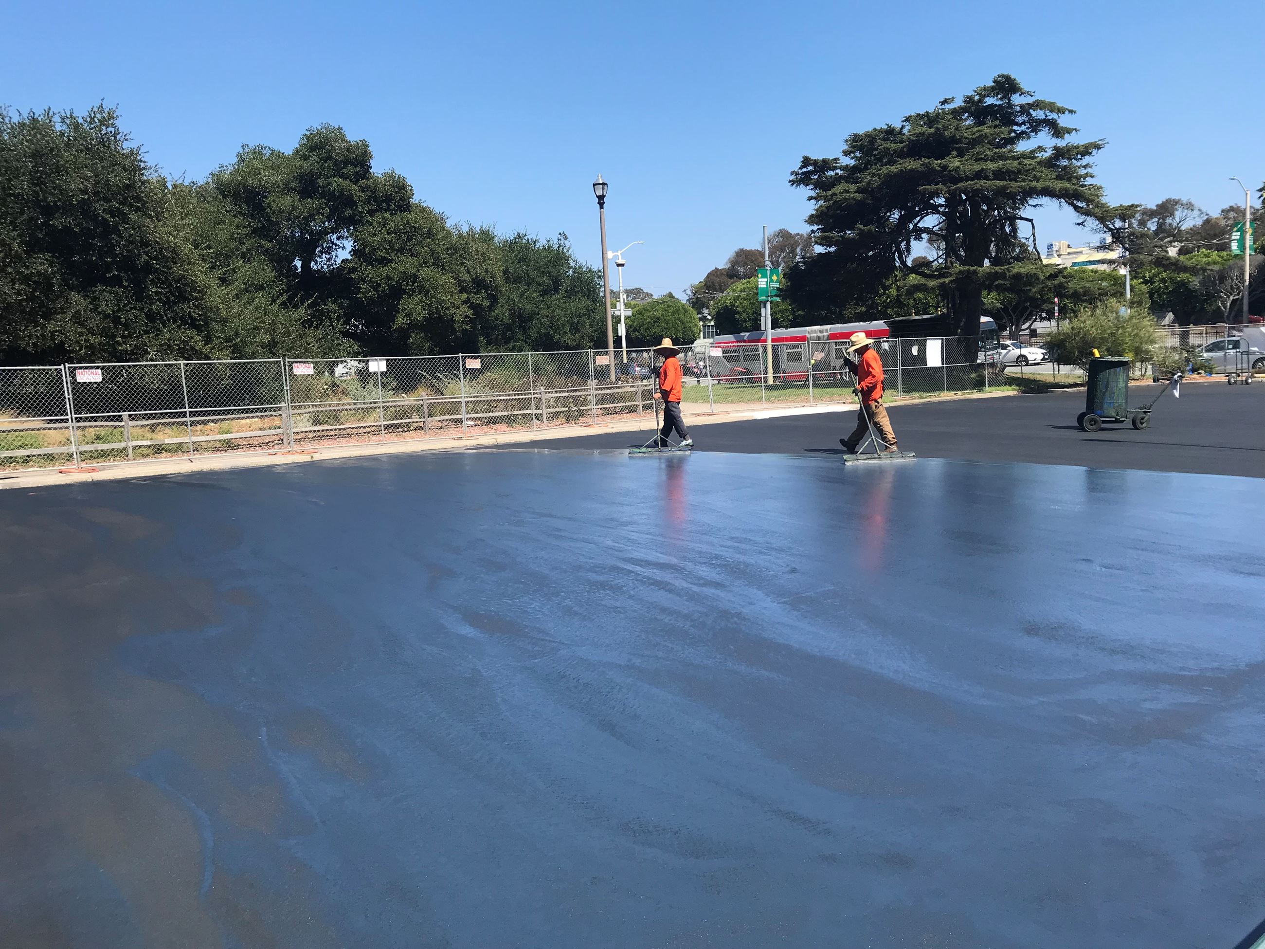 Two construction workers wearing bright orange shown skimming the acrylic coat over the asphalt