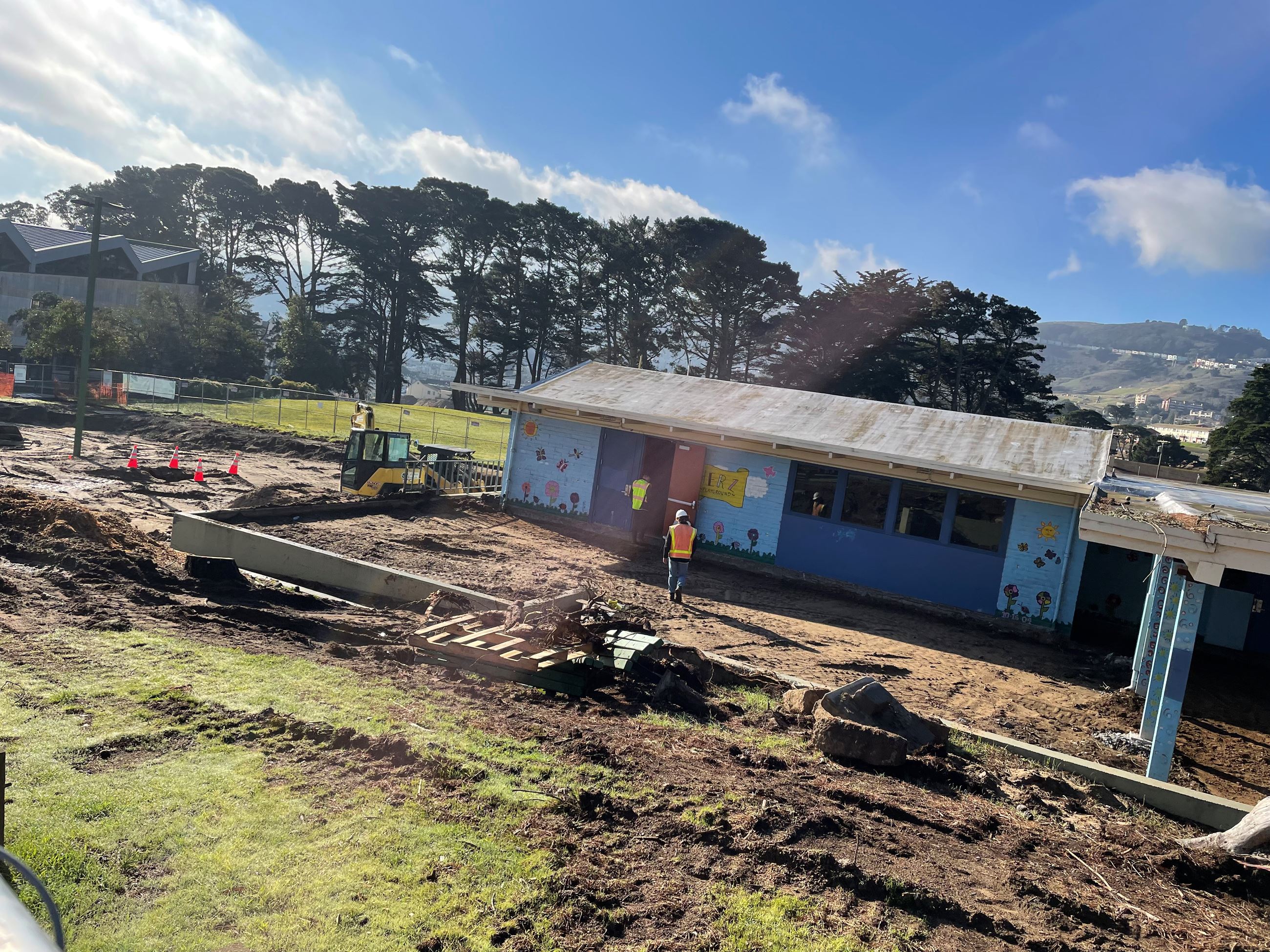 Blue clubhouse shown surrounded by exposed soil, construction workers and equipment.
