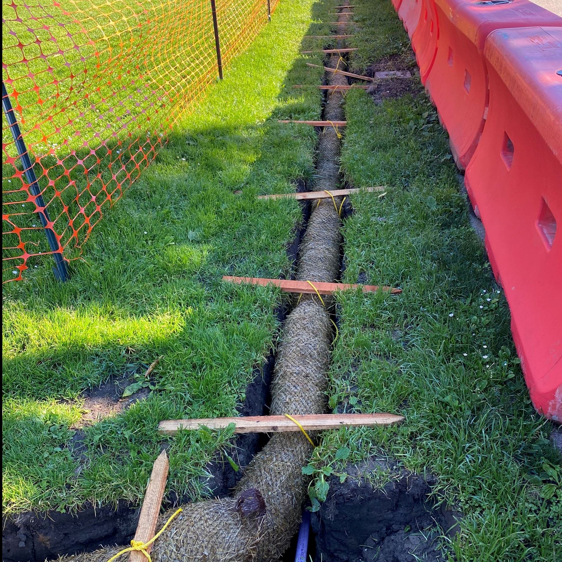 Erosion control waddles shown in the grass surrounded by orange barriers and orange web fencing