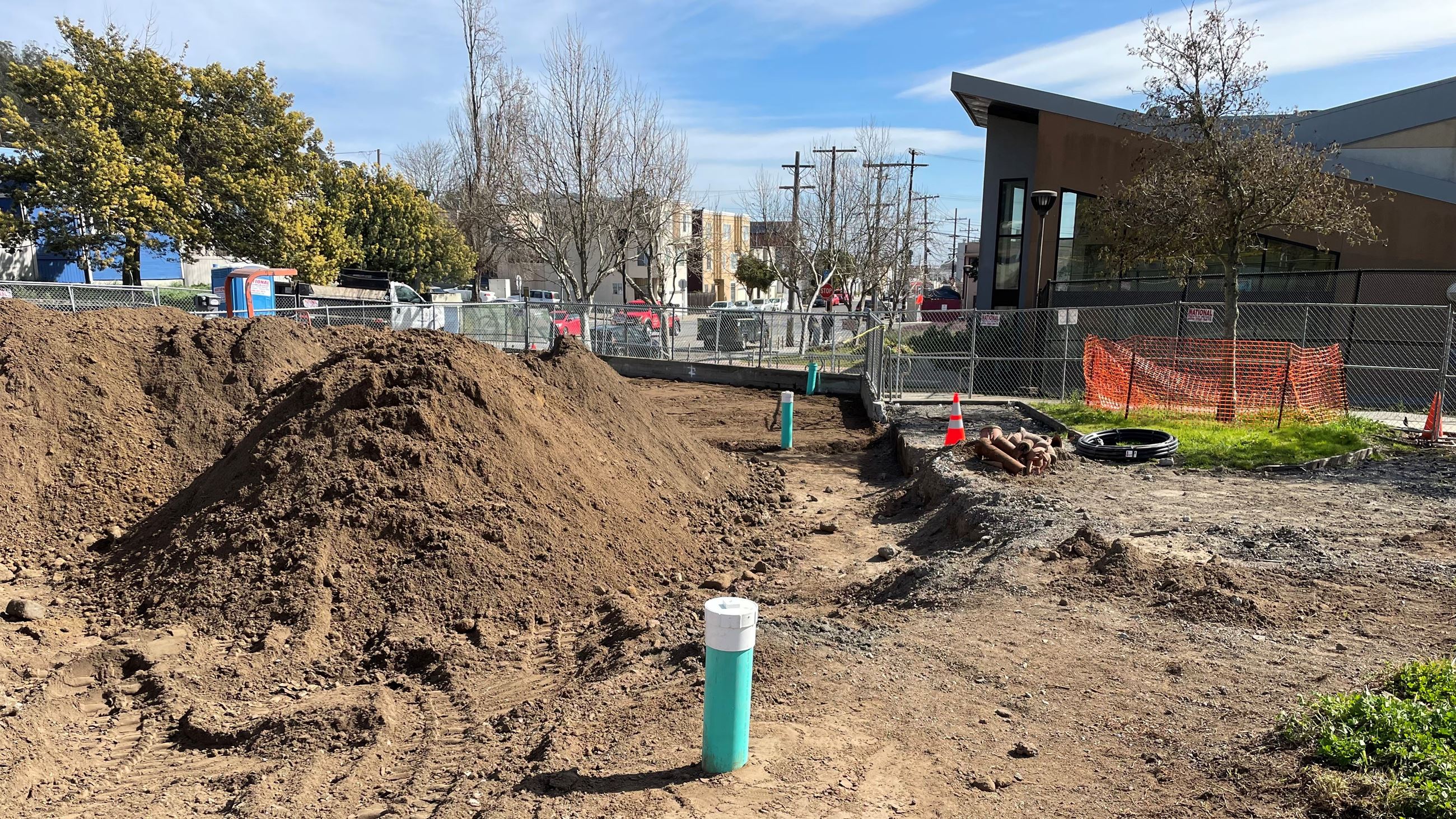 Photo of pile of soil and new pipes at Herz Playground with pool building and neighborhood 