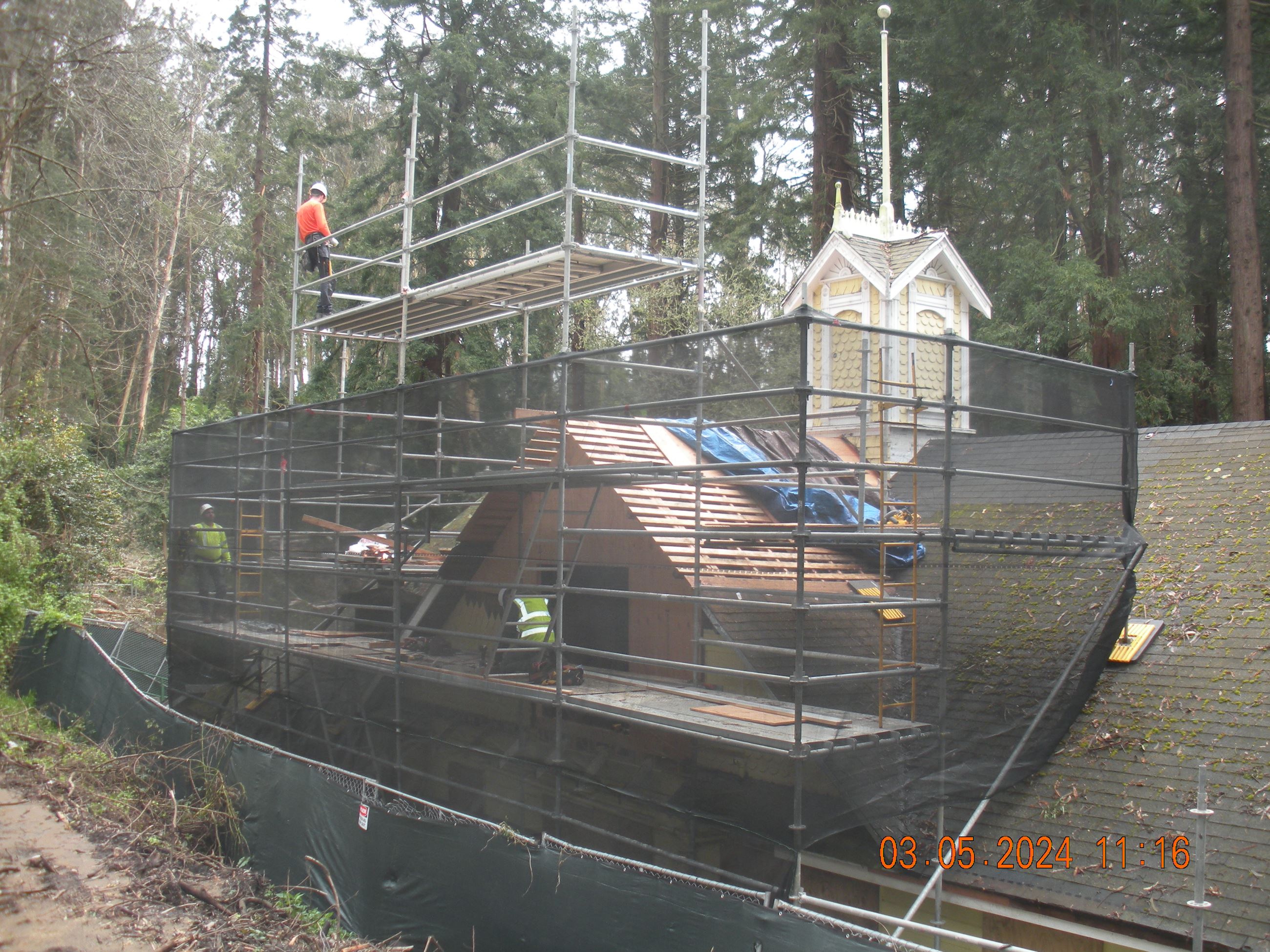 Roofers on scaffolding frame the new sections of roof.