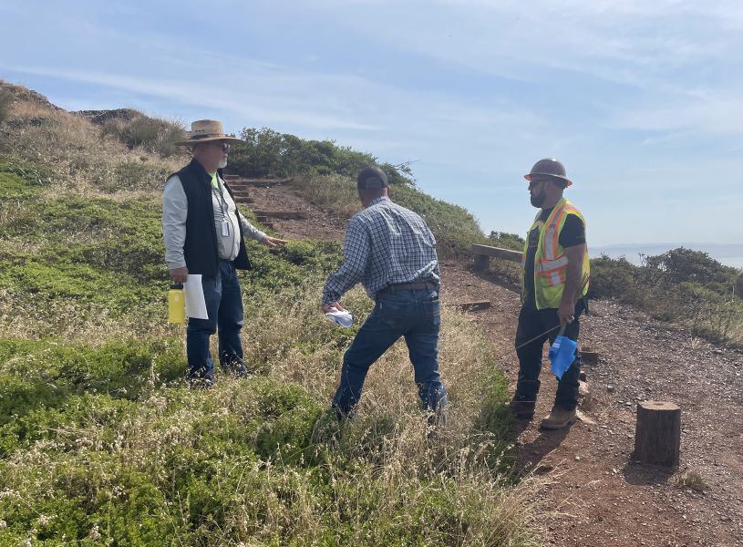 Three workers prepare for trail construction work