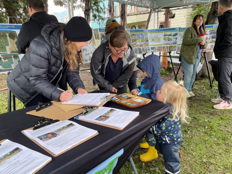 Two staff talk to two young children at event table