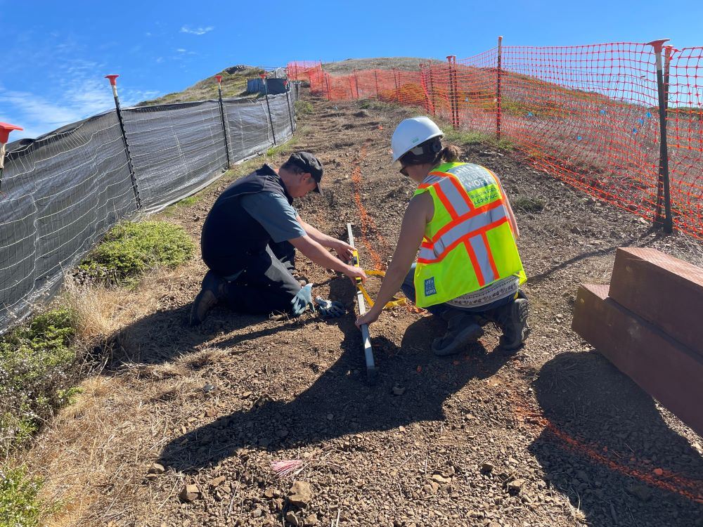 Two workers with a tape measure on the ground at Twin Peaks
