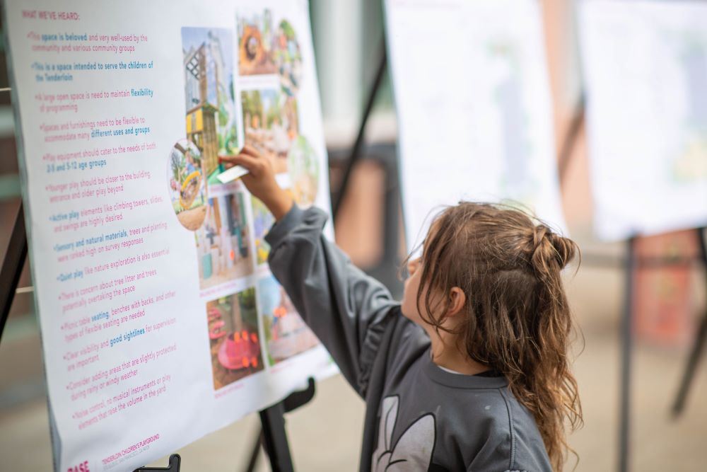 Young child places sticker on concept design board at Tenderloin Rec Center