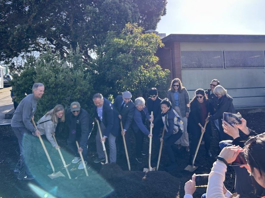 Group of people put golden shovels in soil at ground breaking ceremony